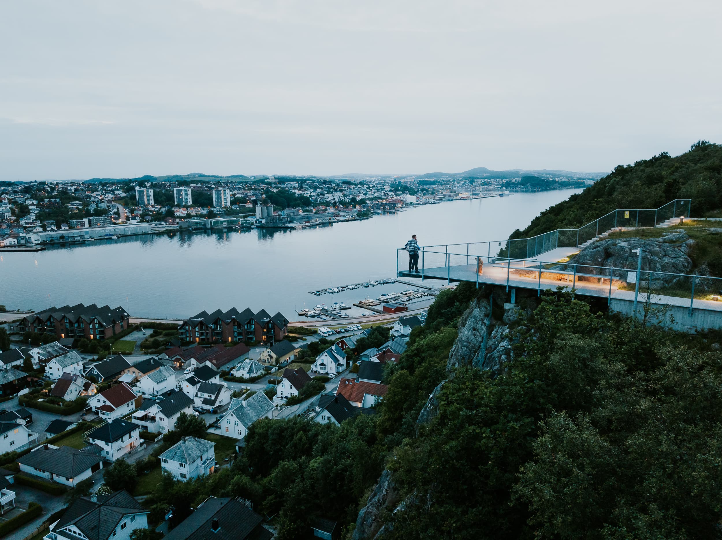 Two people and a dog walking up the stairs to the mountain Hanafjellet. The stairs are called Hanatrappene. From the top the view shows Sandnes and fjord