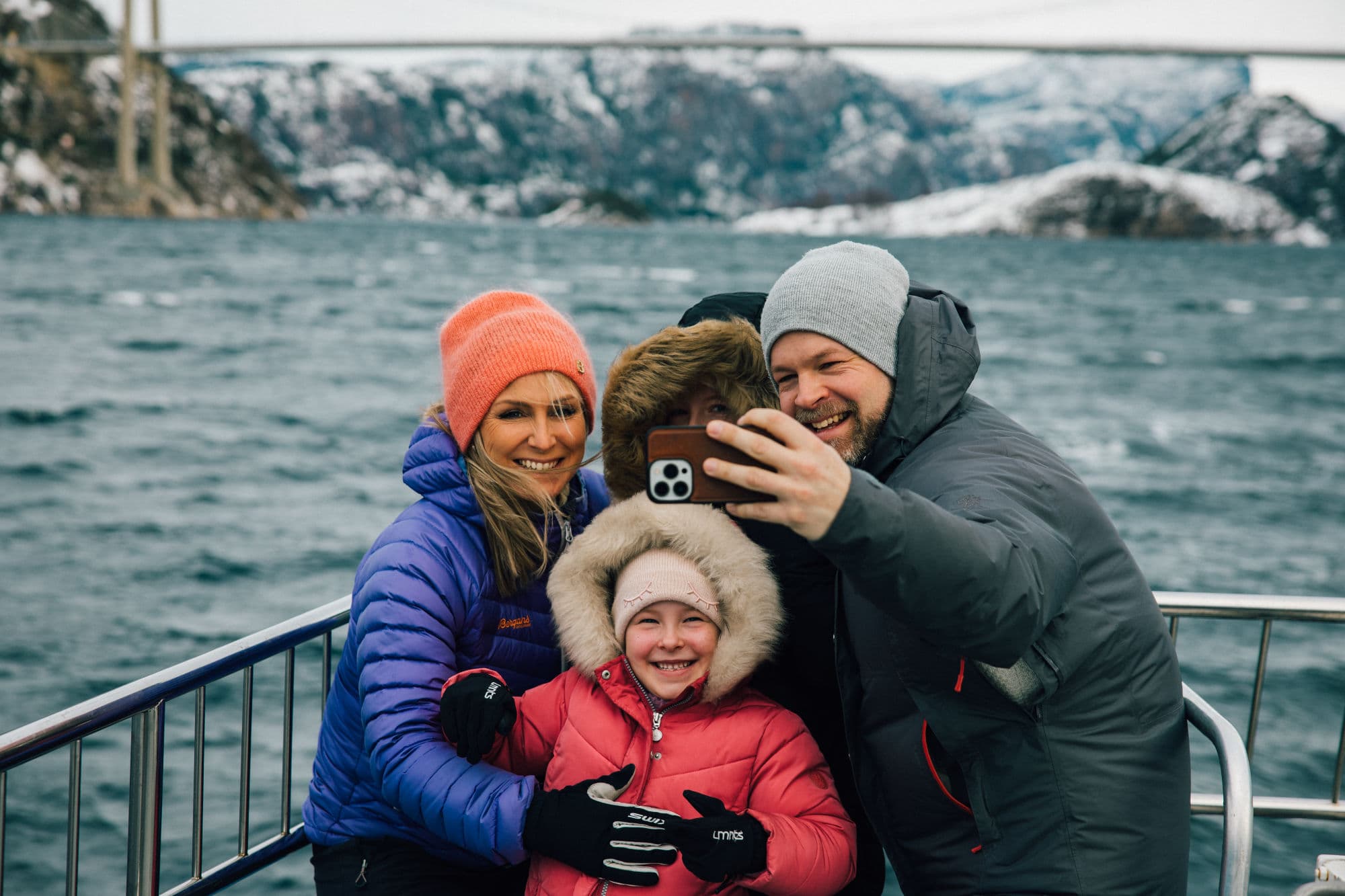 Family on fjord cruise in the Norwegian fjords during winter, beautiful fjord scenery, family taking pictures from sightseeing boat, mountainsides with snowcapped tops