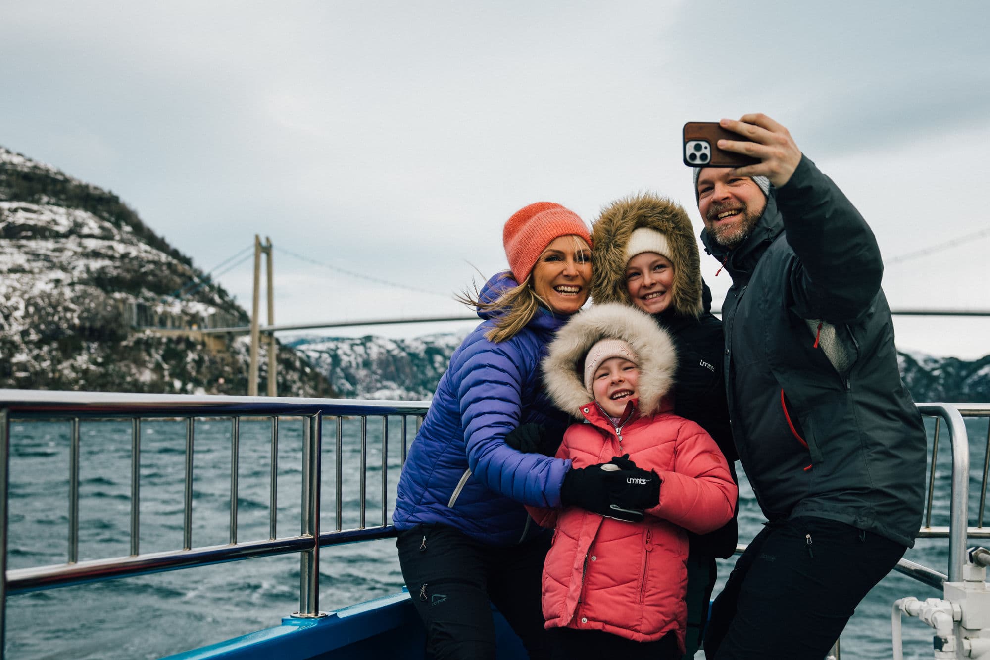 Family on fjord cruise in the Norwegian fjords during winter, beautiful fjord scenery, family taking pictures from sightseeing boat, mountainsides with snowcapped tops
