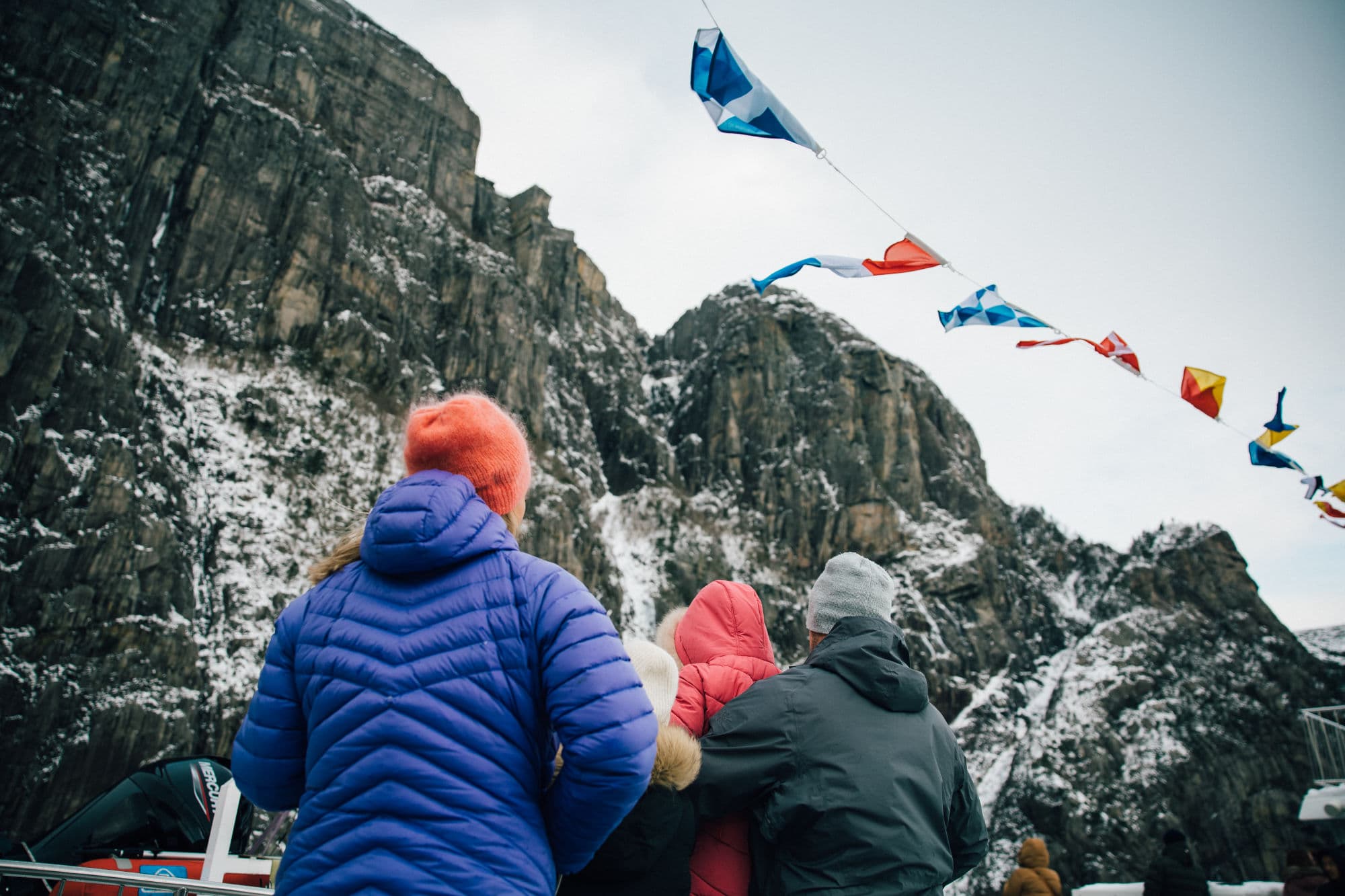 Family on fjord cruise in the Norwegian fjords during winter, beautiful fjord scenery, family taking pictures from sightseeing boat, mountainsides with snowcapped tops