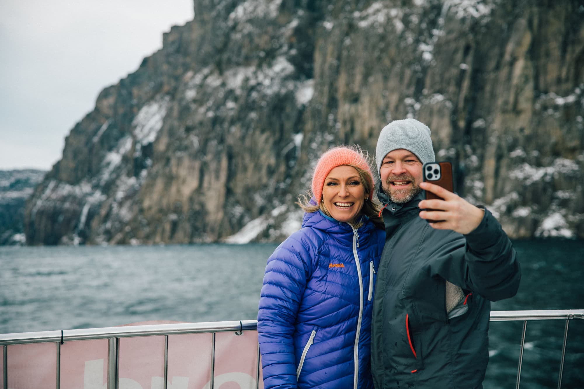 Family on fjord cruise in the Norwegian fjords during winter, beautiful fjord scenery, family taking pictures from sightseeing boat, mountainsides with snowcapped tops