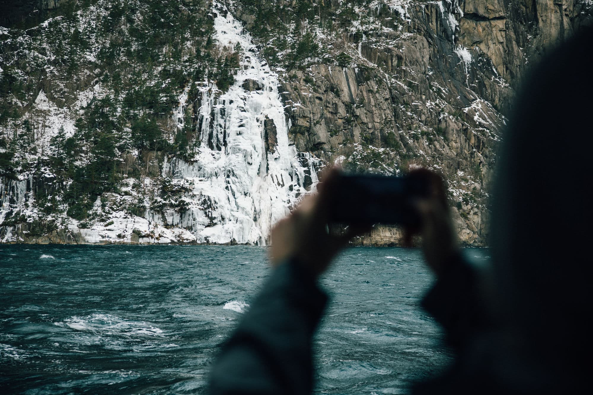 Family on fjord cruise in the Norwegian fjords during winter, beautiful fjord scenery, family taking pictures from sightseeing boat, mountainsides with snowcapped tops