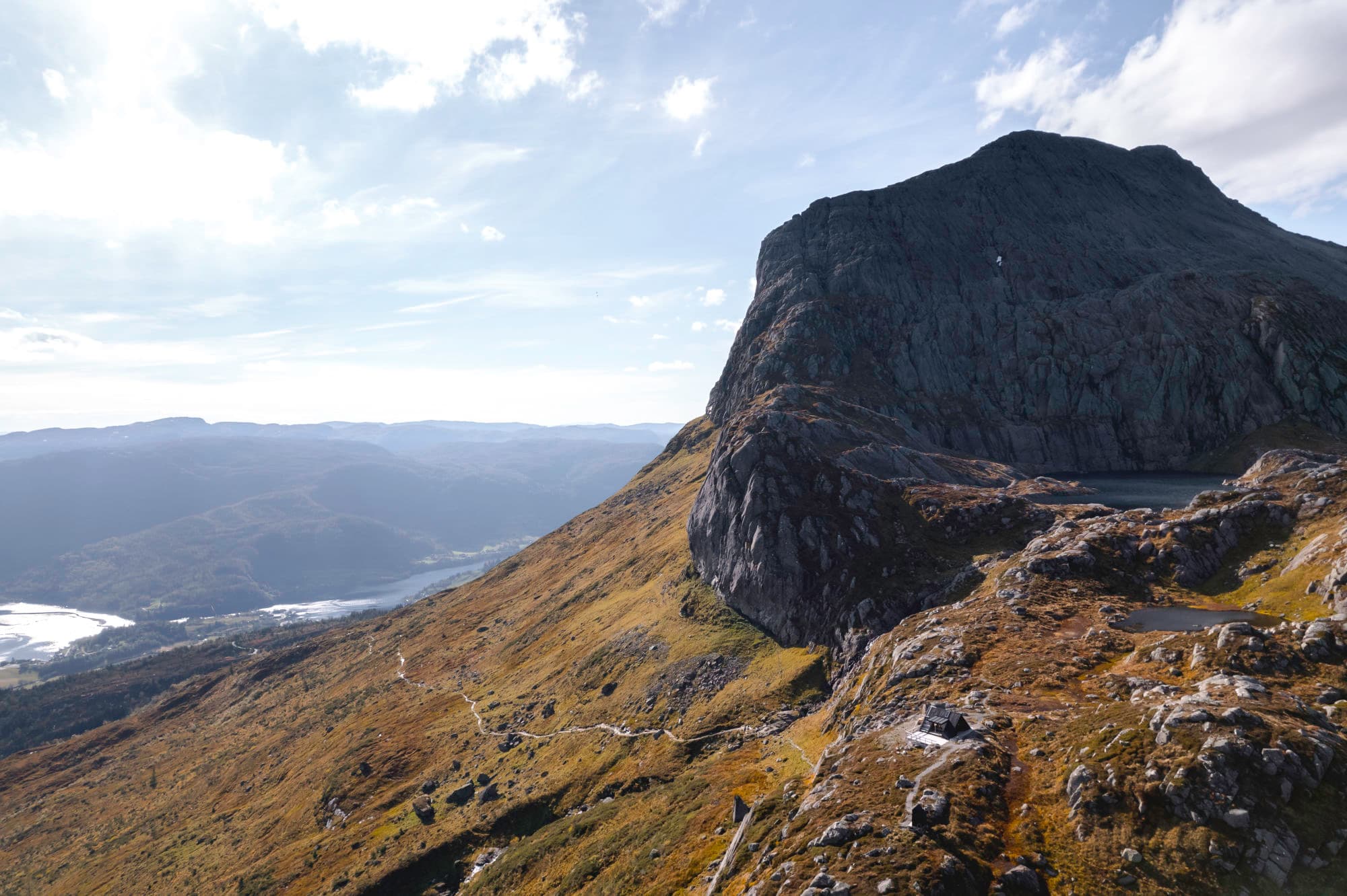 et stort fjell med hytte på ene siden. et hav nede i botn