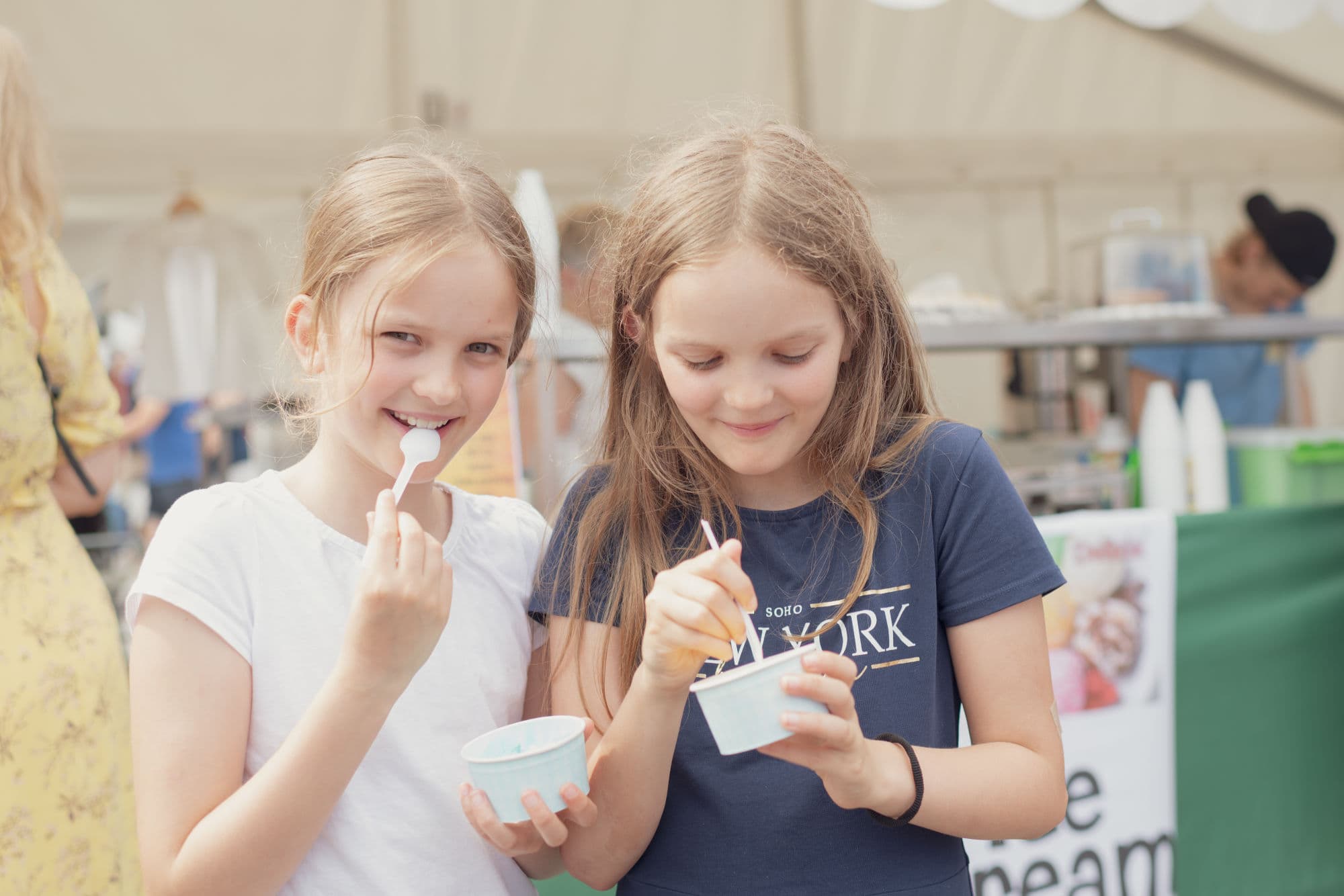 Two girls eating something from a paper bowl and smiling