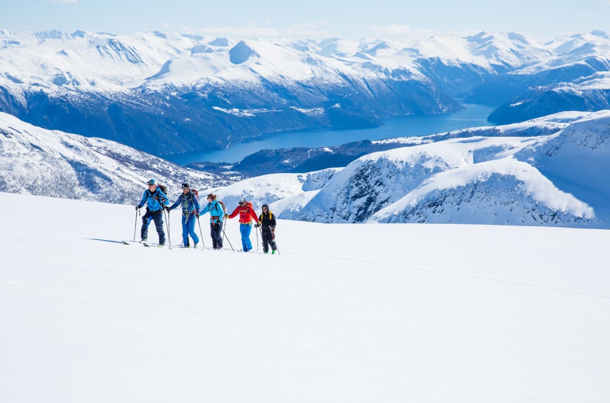 5 personer på fjelltur med ski, utsikt til fjell og fjord i bakgrunnen.