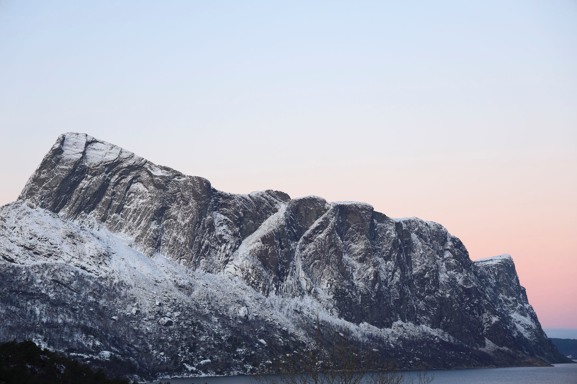 Liheste er dekka med snø Bak fjellet er det en raud himmel - solnedgang. Fjellet stuper ned i sjøen. Foto