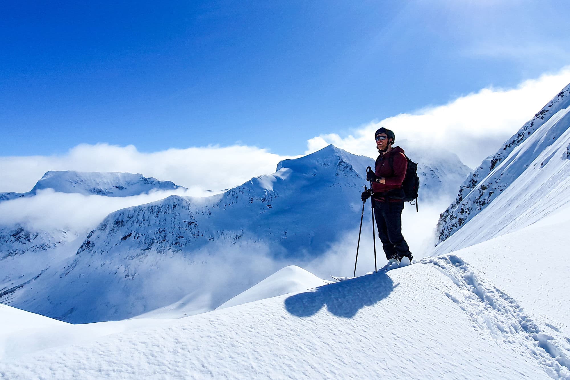 Person på topptur med ski og kvite fjell i bakgrunnen.