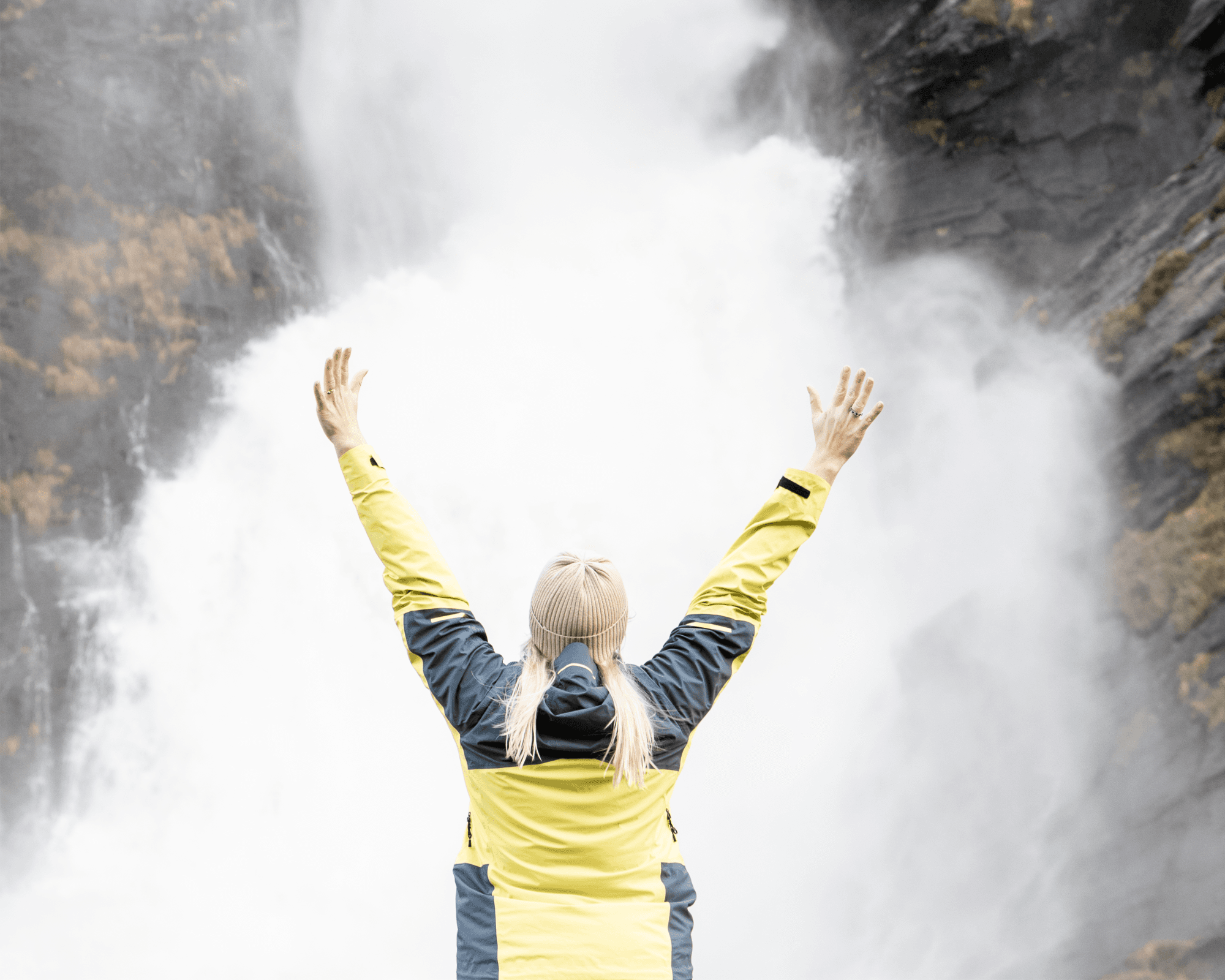 person som står med hendene opp framfor ein foss.