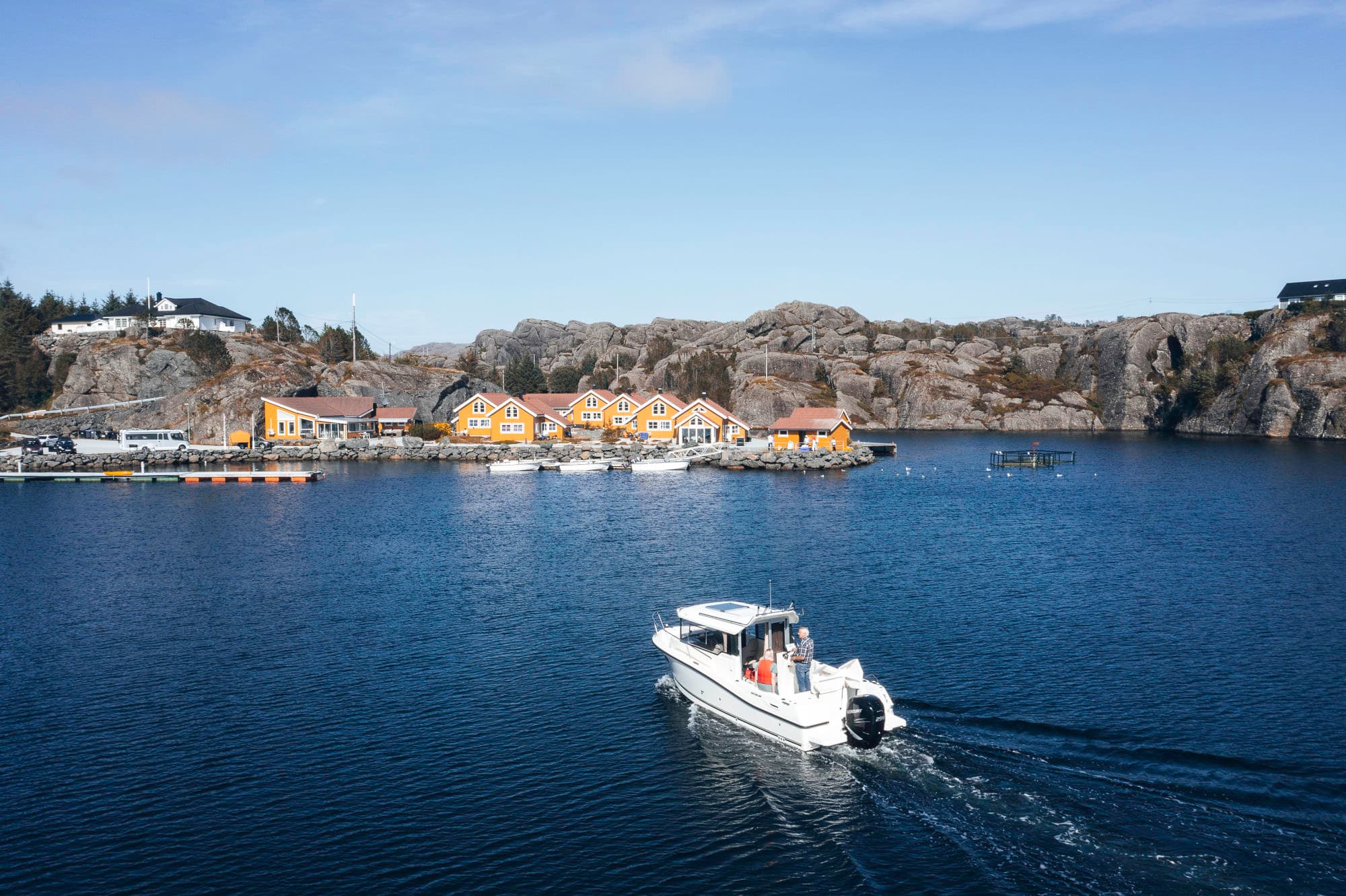 en båt er på veg inn til kaia. det er mange gule hus ved kaien, og det er fjell rundt.