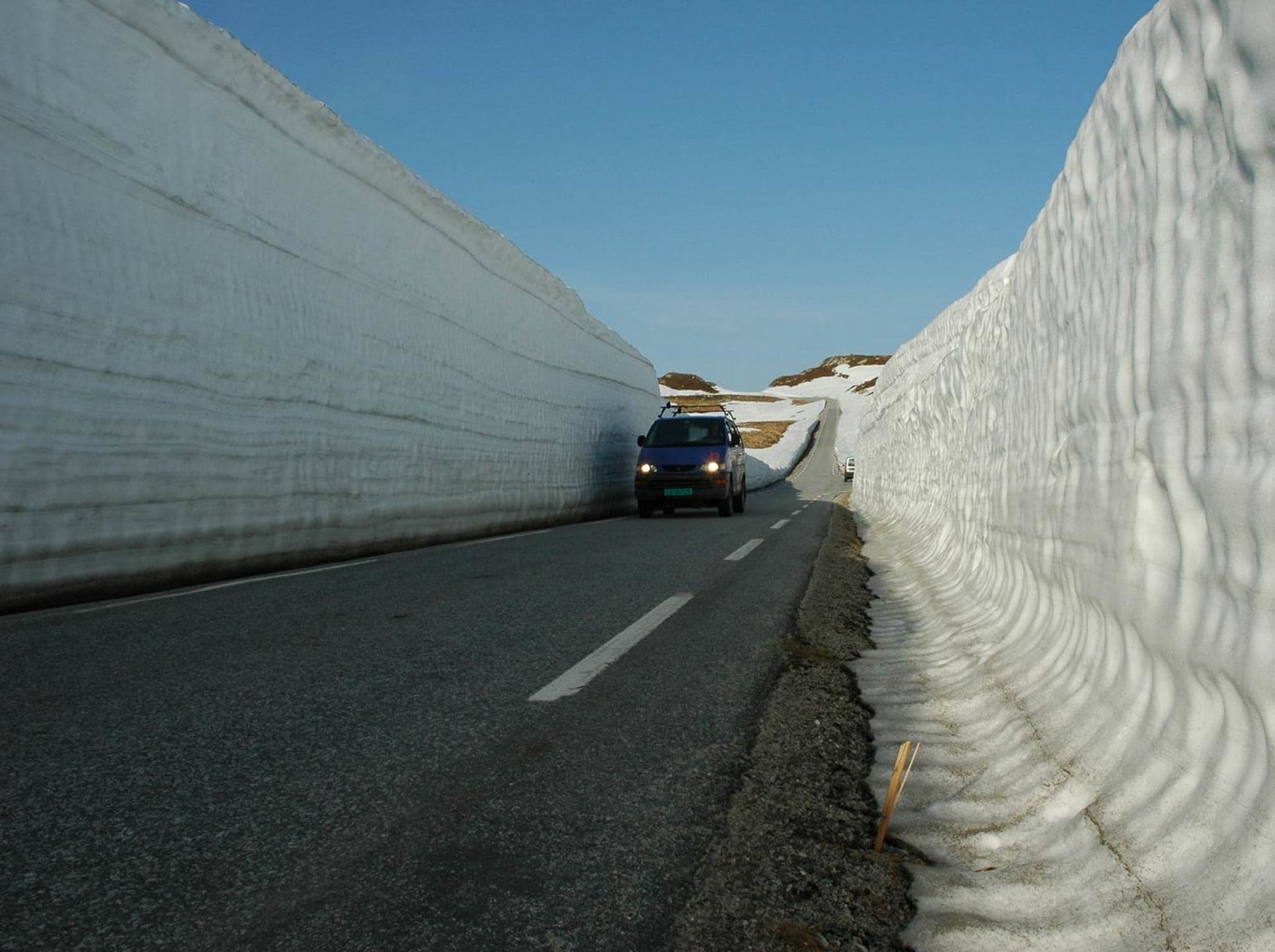 Car driving on a road with high snowbanks on each side.