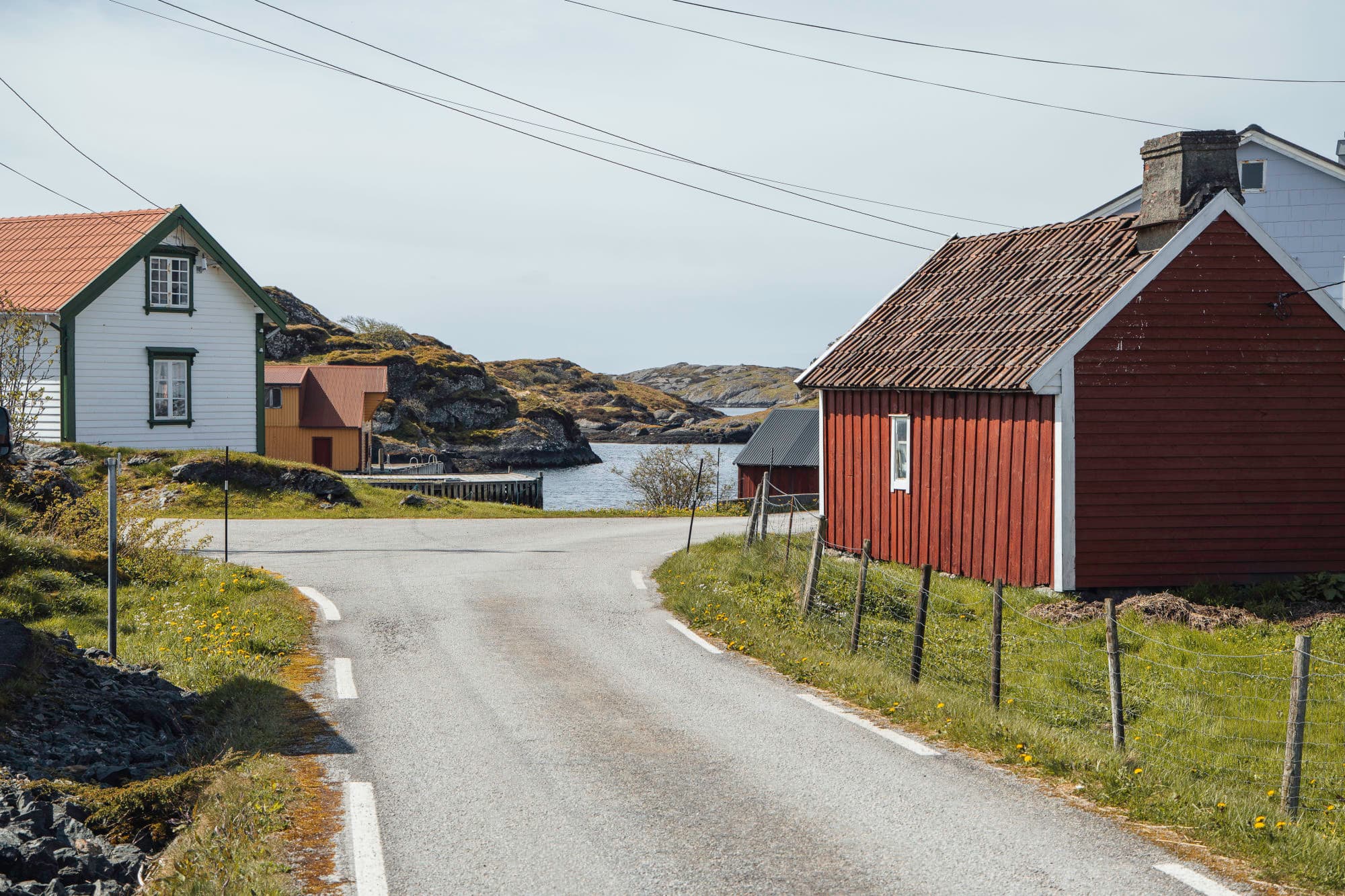 sjøhus og andre hus som står langs ein veg. sjøen er i enden av bildet. ei gul sjøhus vises bakom eit kvitt hus med grøne detaljer