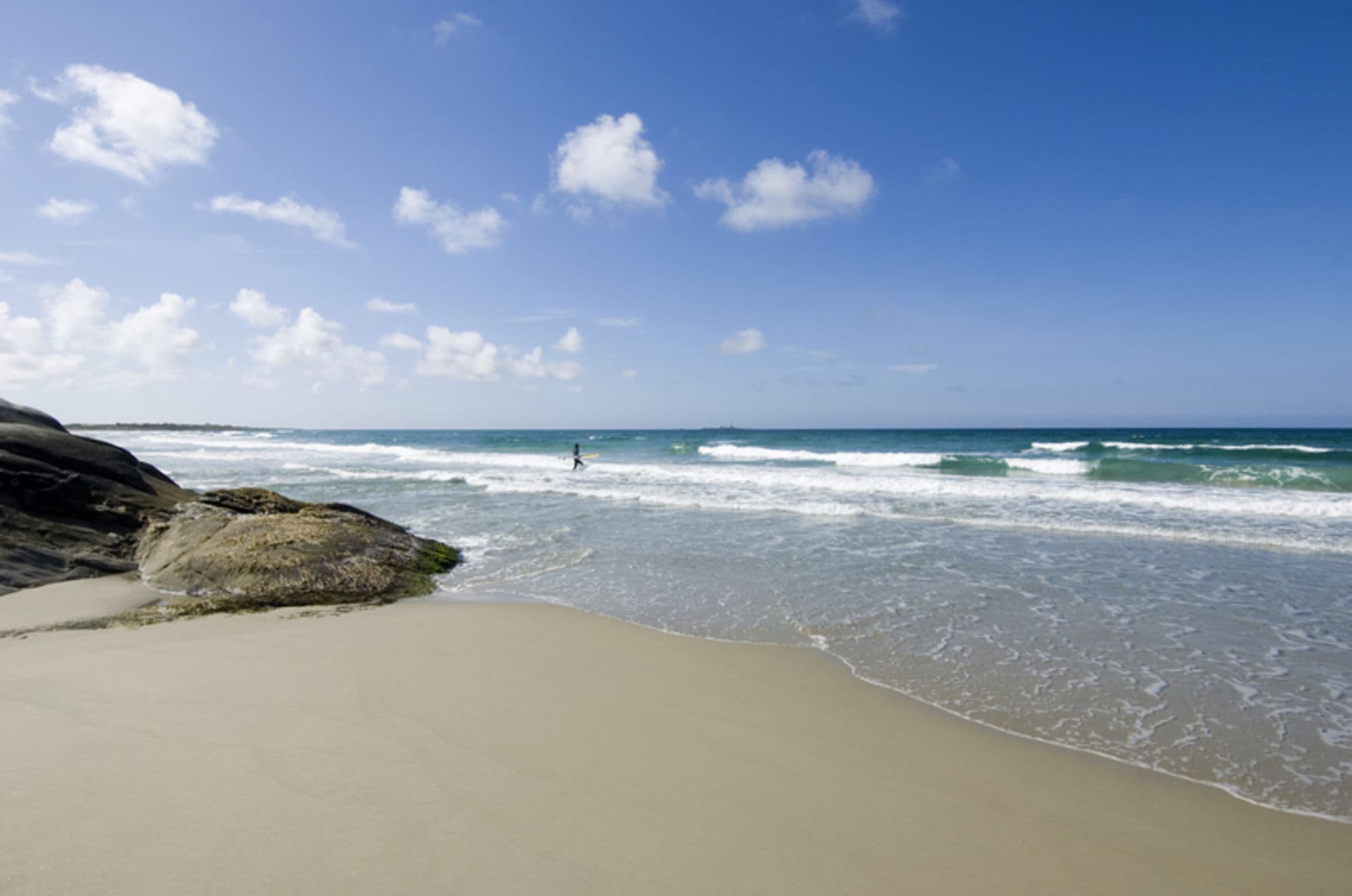 clear day, blue sky, surfer headed out for the water Hellesto stranden beach Stavanger