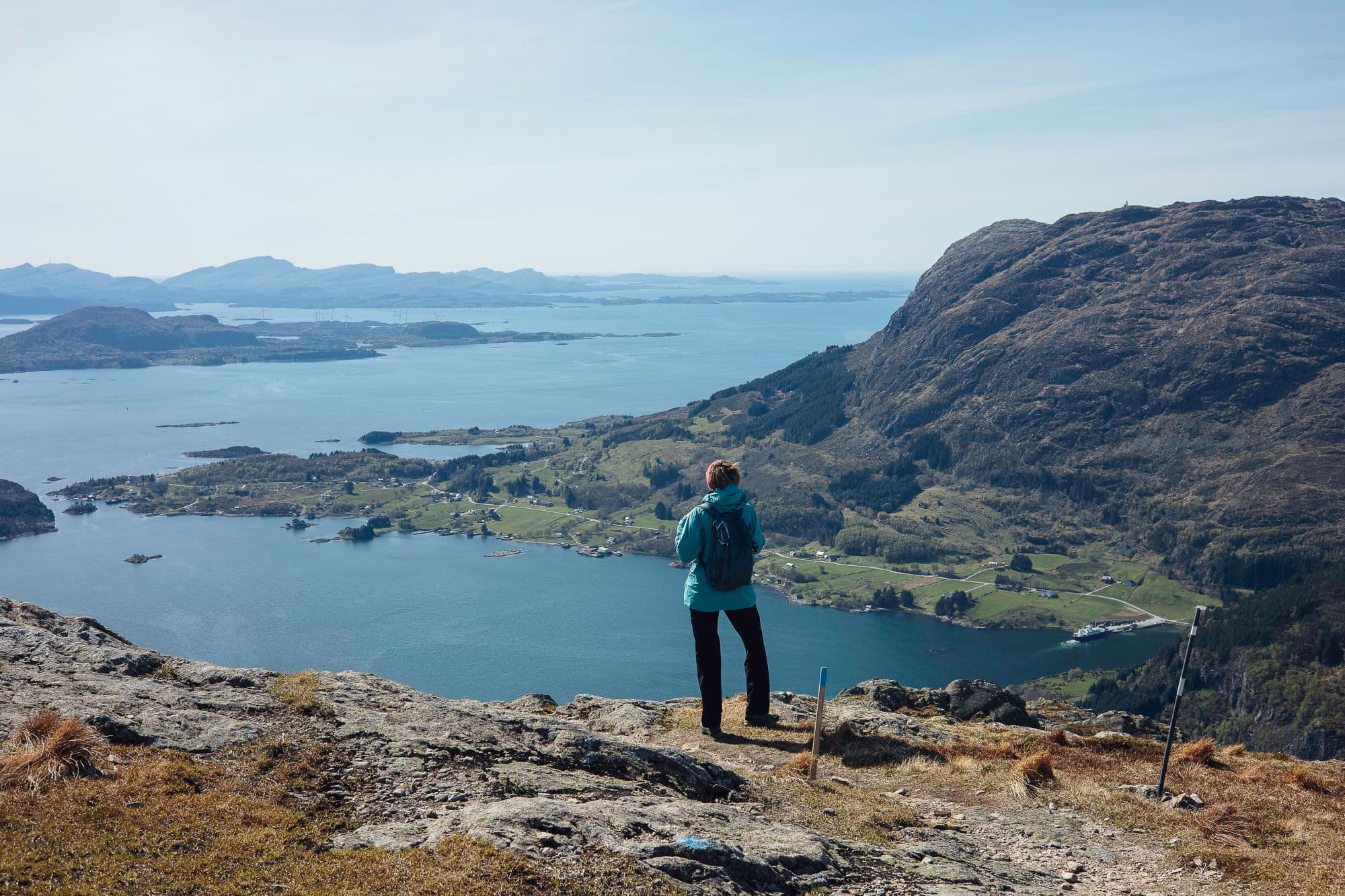 ei dame står og ser ut over utsikten. det er fjell, fjord og hav