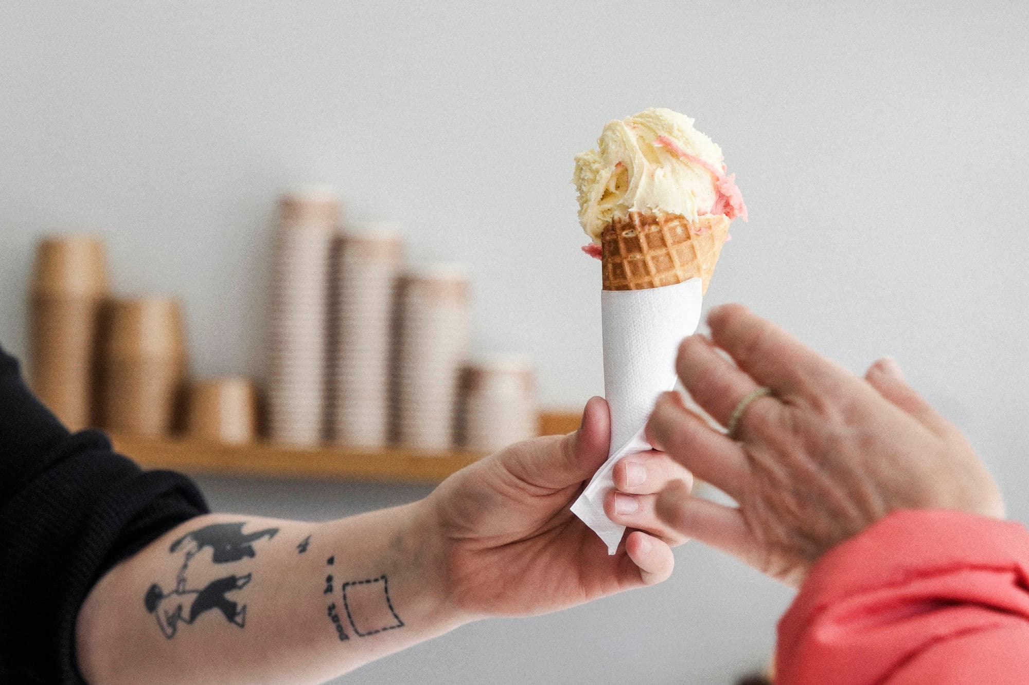 A hand holding an ice cream and handing it over to a customer's hand at ice cream place Siddis Gelato in Stavanger