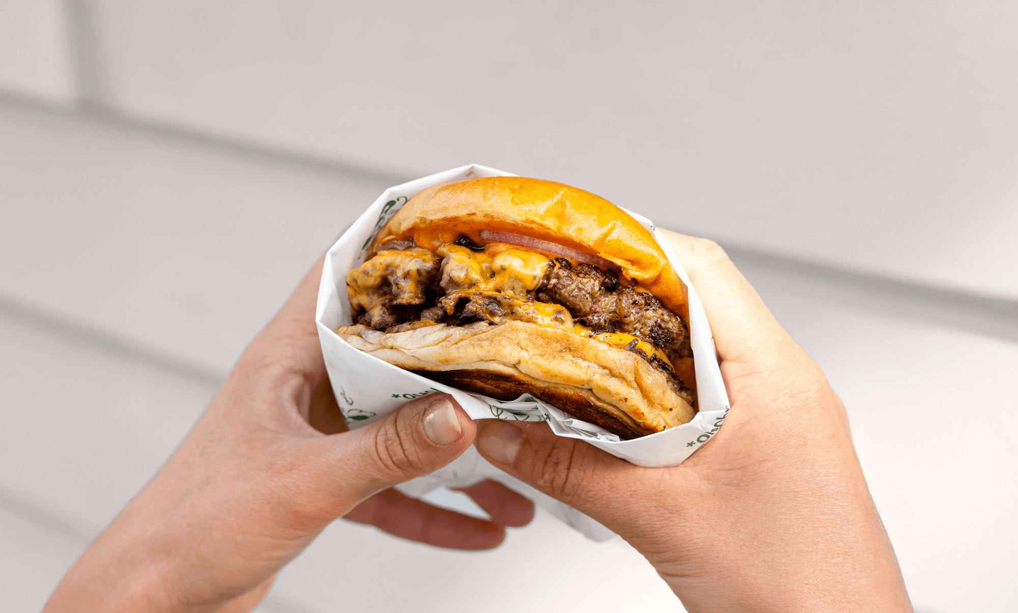 Two hands holding a cheese burger wrapped in napkin