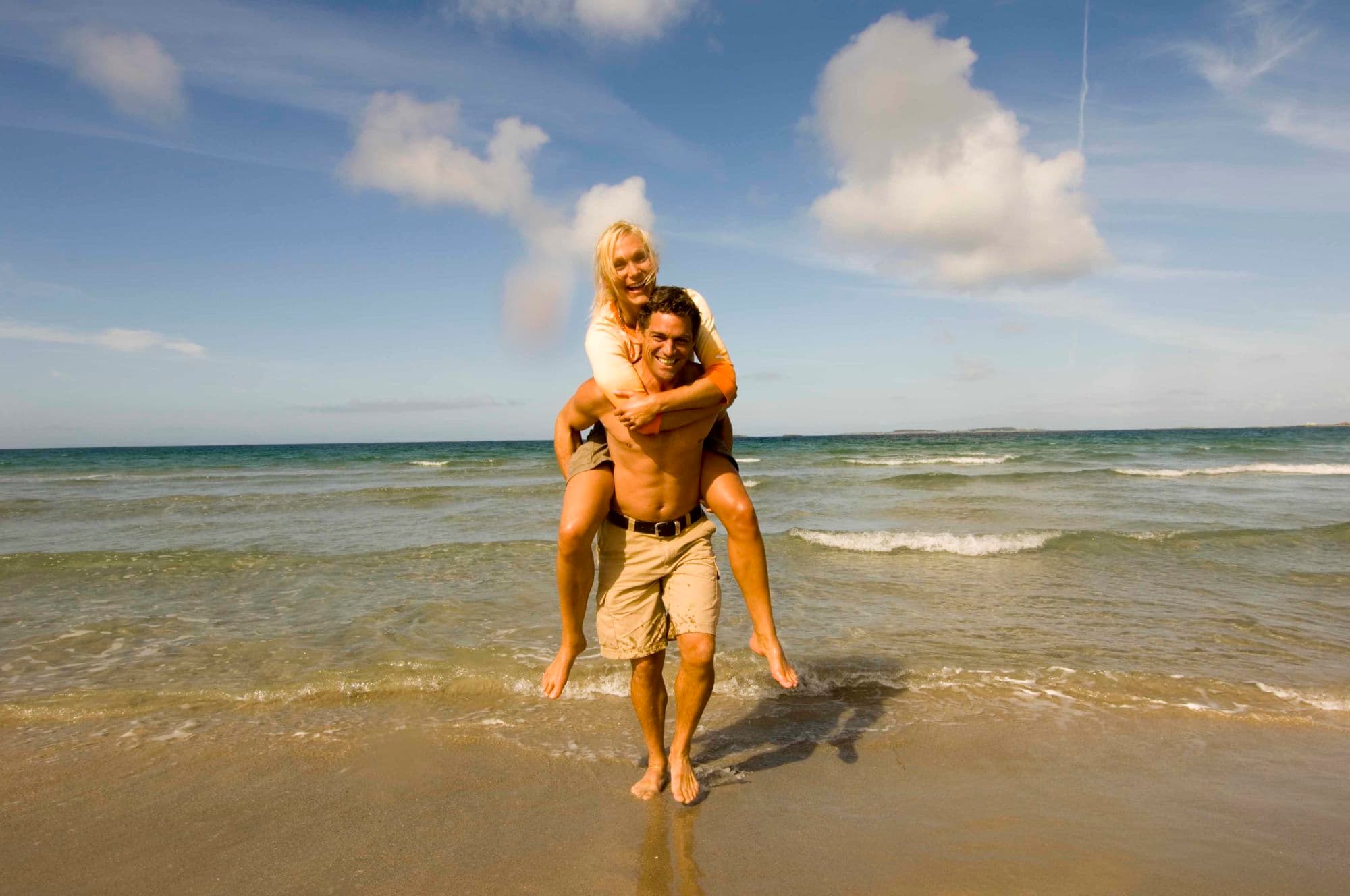 Mann bærer dame på ryggen på stranden.