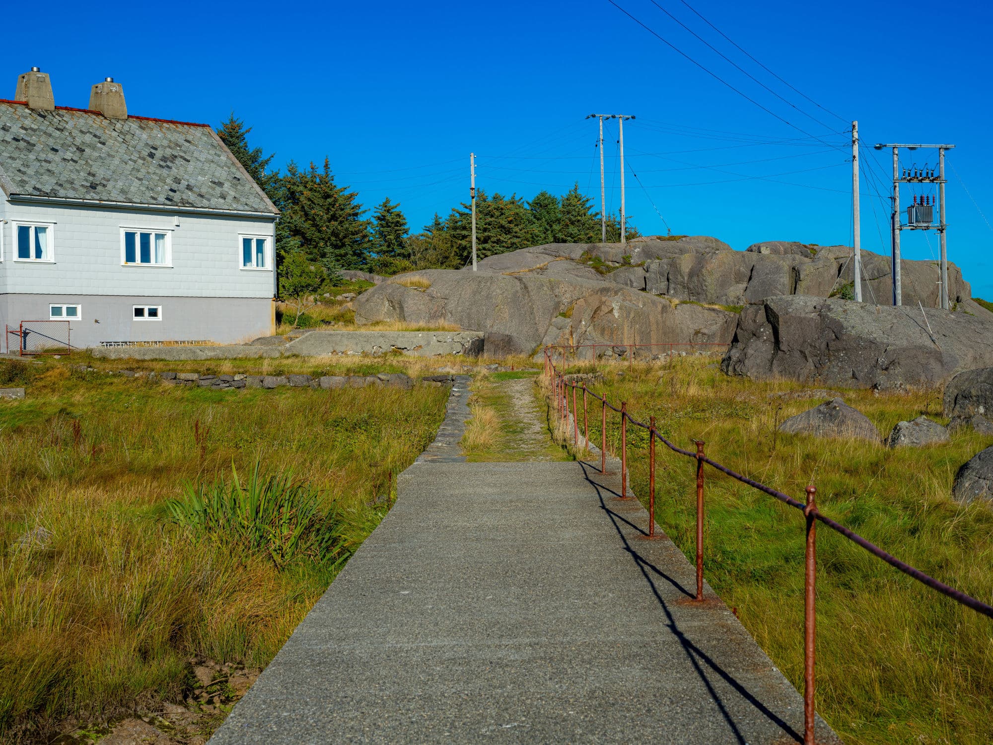 Eigerøya walking to the lighthouse wooden path, and house, grass with autumn colours and rocks.