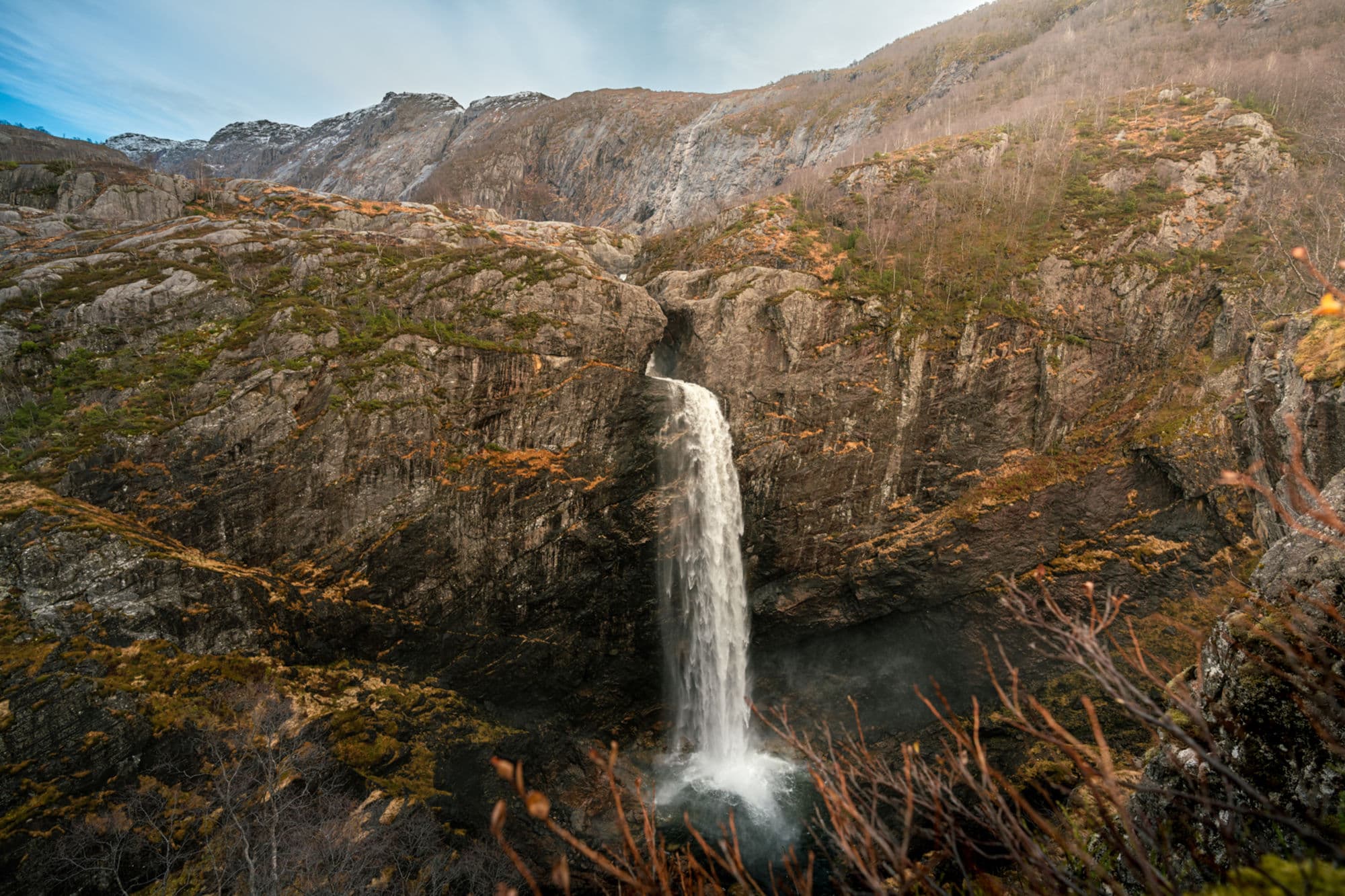 The waterfall Månafossen cascading down the mountainside. The mountain is in autumn colours.