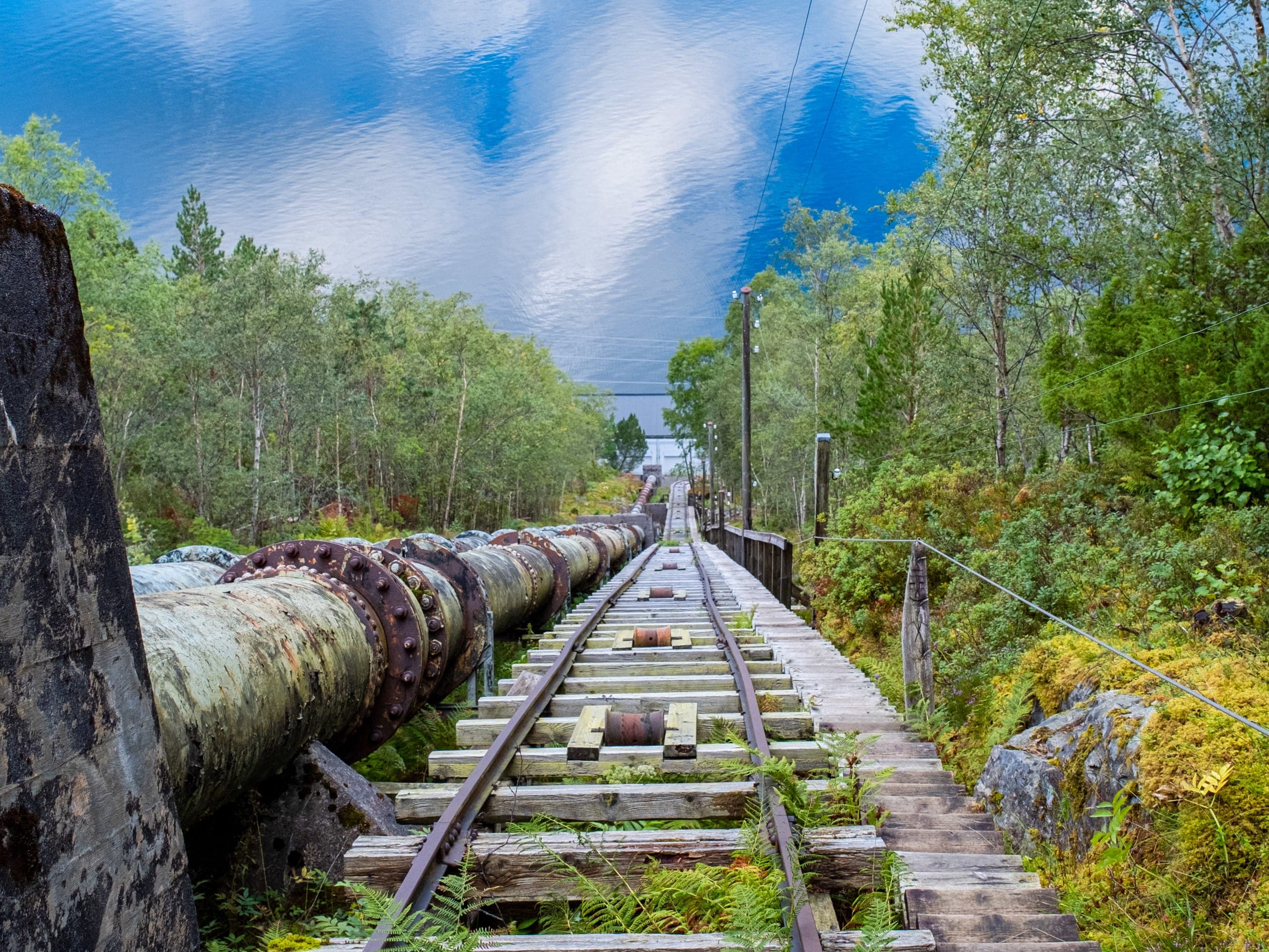 Flørlitrappene sett fra oven og ned mot fjorden. Bratte tretrapper og den blanke fjorden i bunn - himmelen og skyene speiler seg i fjorden. Grønne trær langs trappene.