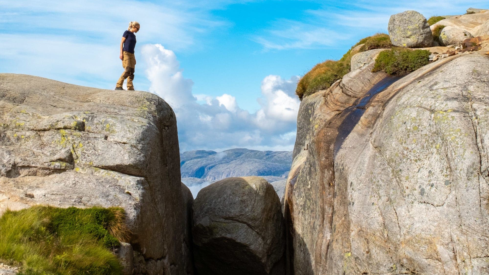 lady standing on top of mountain top looking down on the Kjerag boulder