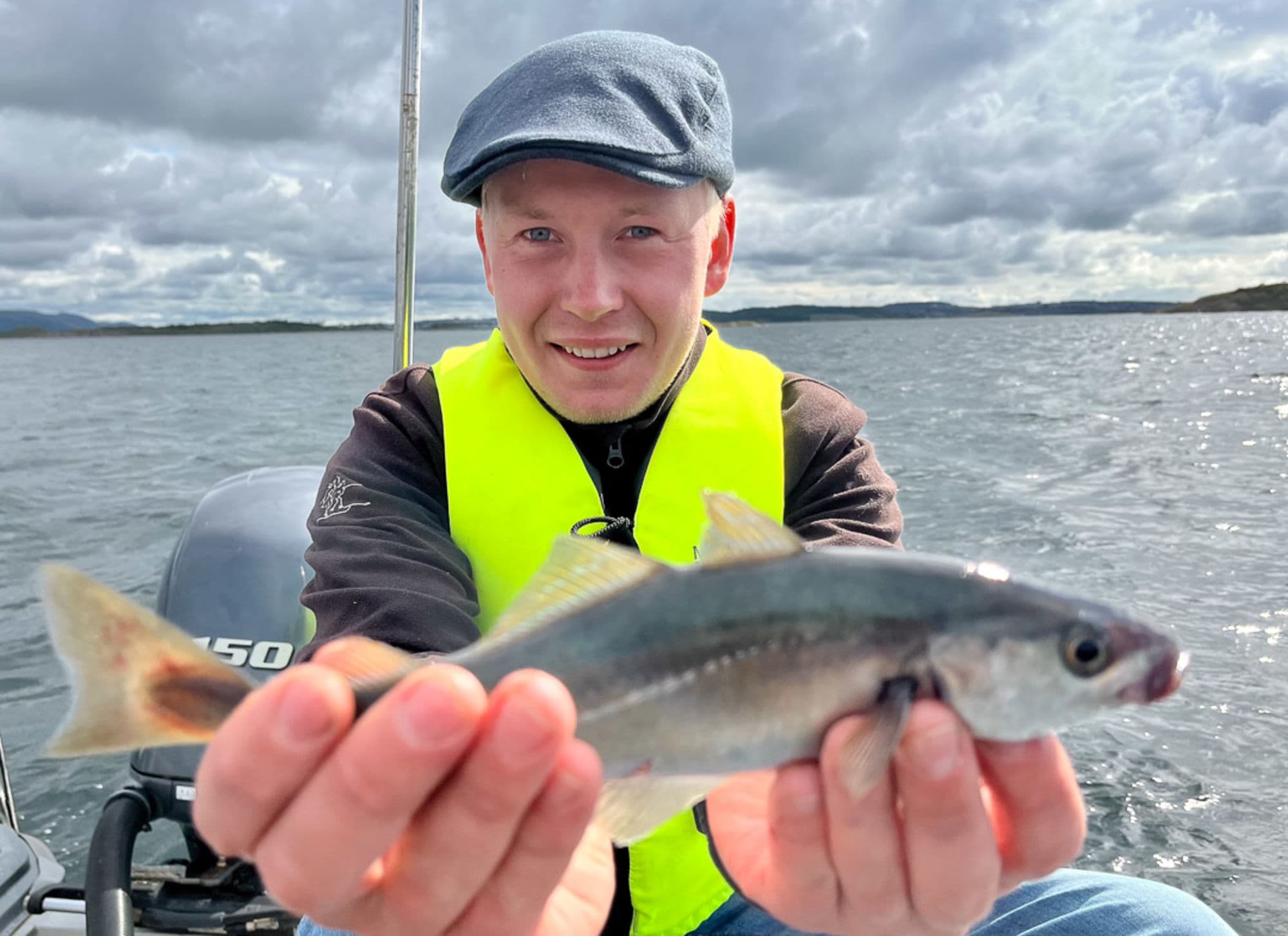 Man holding fish with both hands while sitting in a boat. the sea is behind him.