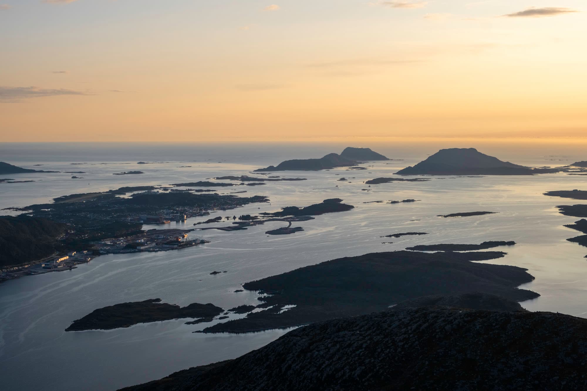 oversiktsbilde av ein by som ligg heilt i kanten av storhavet. det er øyer rundt byen. det er solnedgang, og eit flatt hav